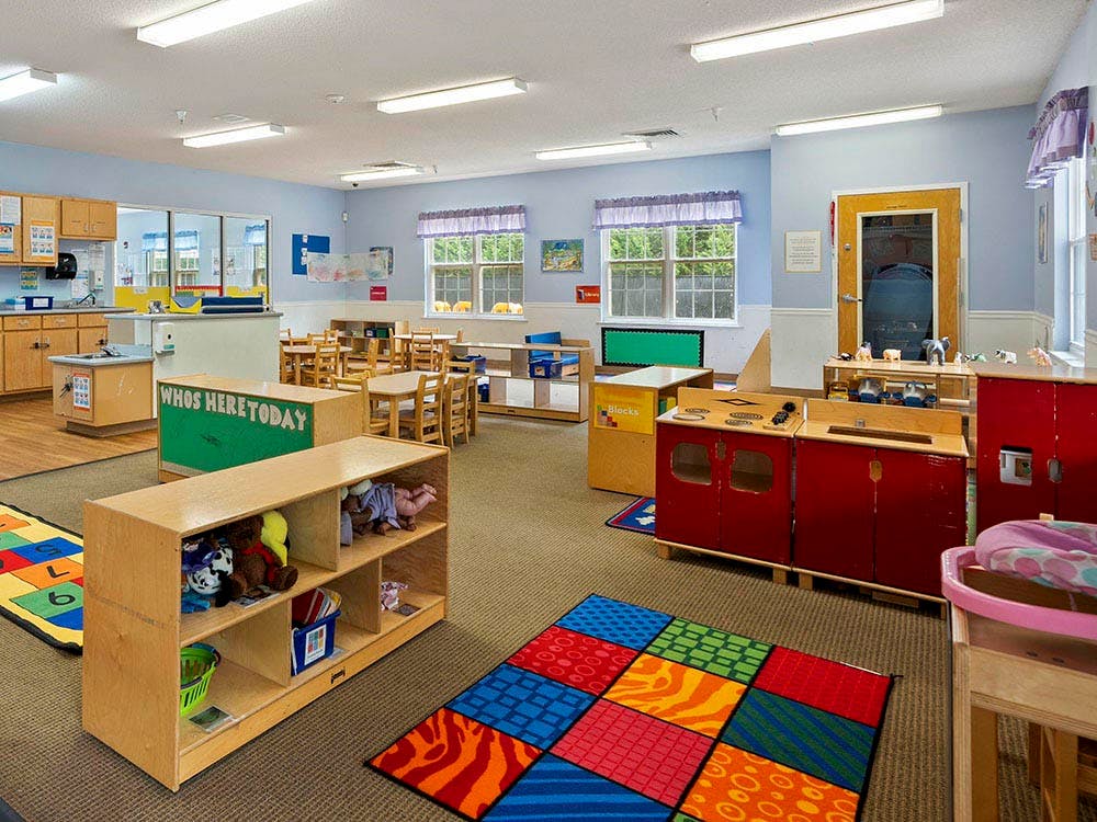 Childcare classroom with colorful rugs, small tables, and play areas