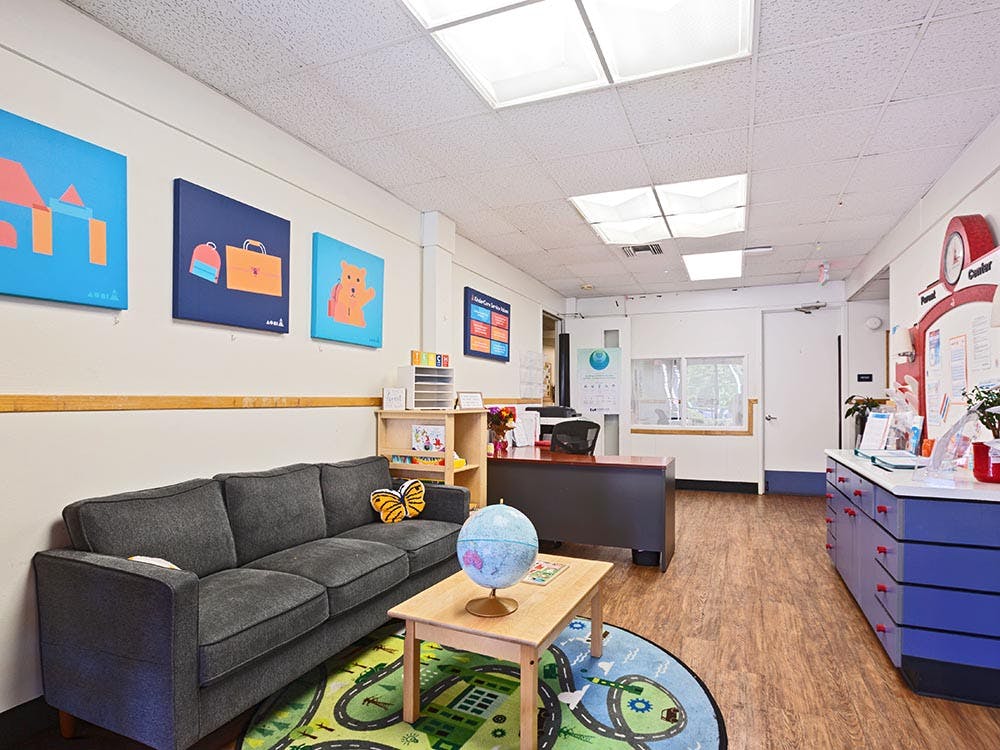 An office waiting area with a gray couch, rug, small table, and reception desk