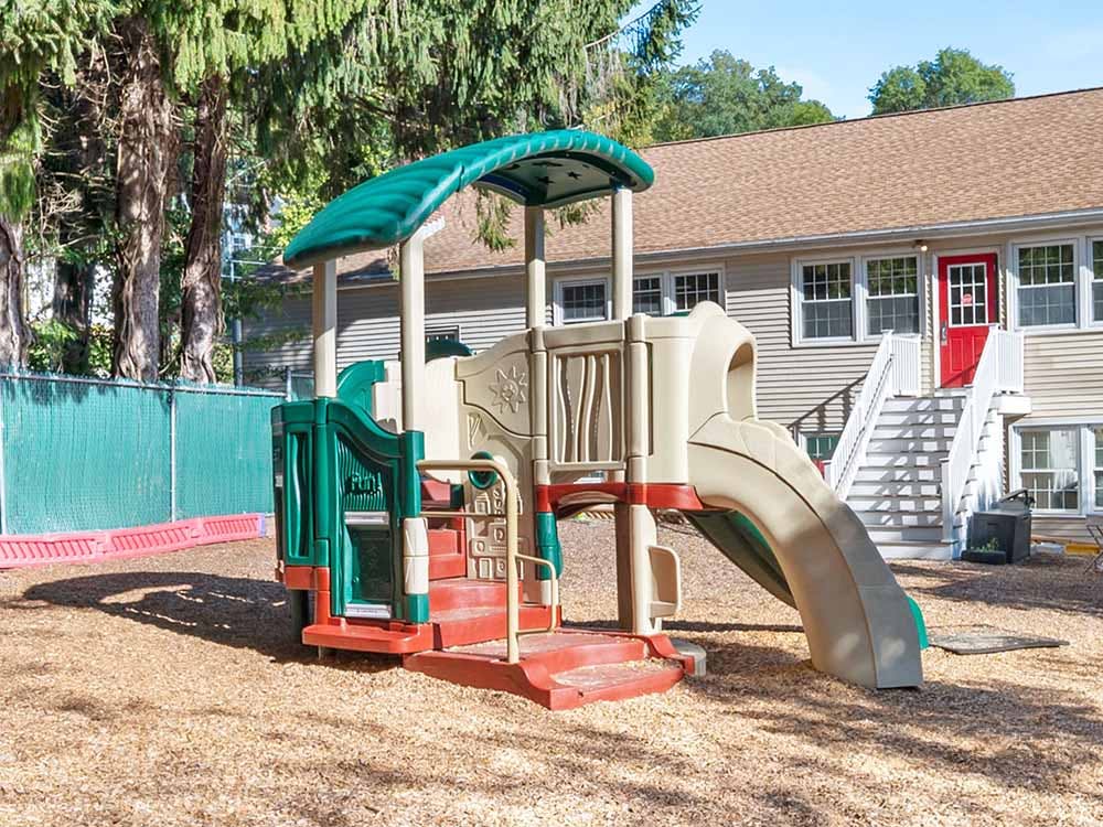 A beige and green plastic playground set with a slide on wood chips