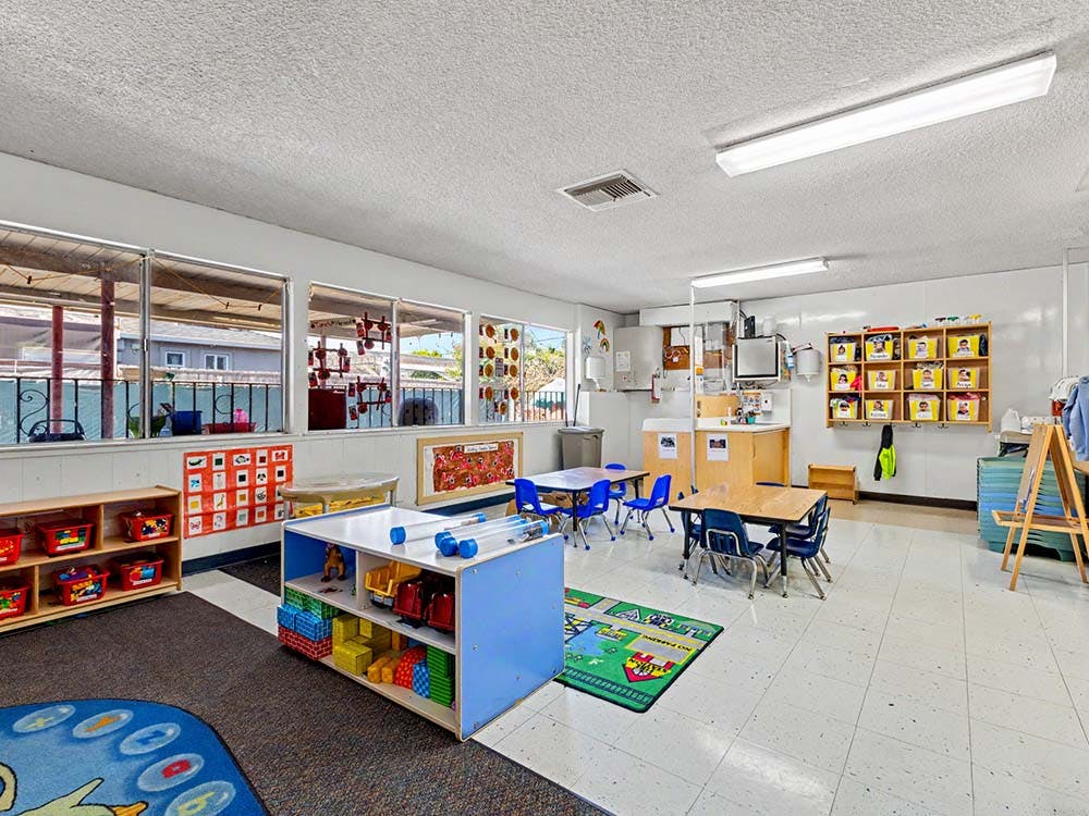 Classroom with child-sized tables and chairs, storage shelves, and large windows