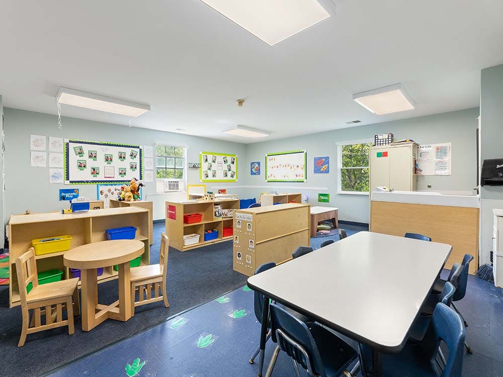 Classroom with child-sized tables and chairs, shelves with toys and bins