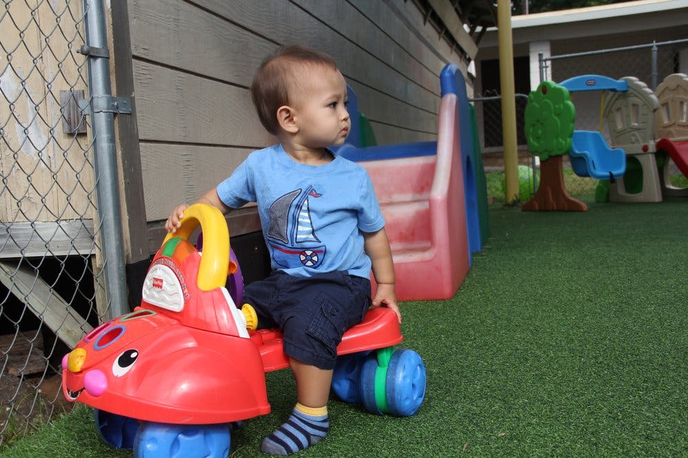 Child sitting on a red ride-on toy on artificial grass