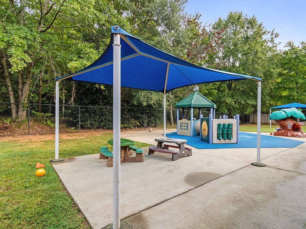 A covered outdoor play area with play structures and small picnic tables