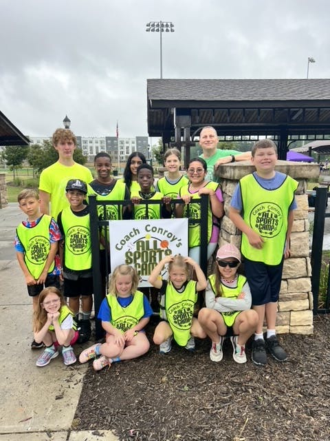 Group of children and adults posing with a "Coach Conroy's All Sports Camp" sign