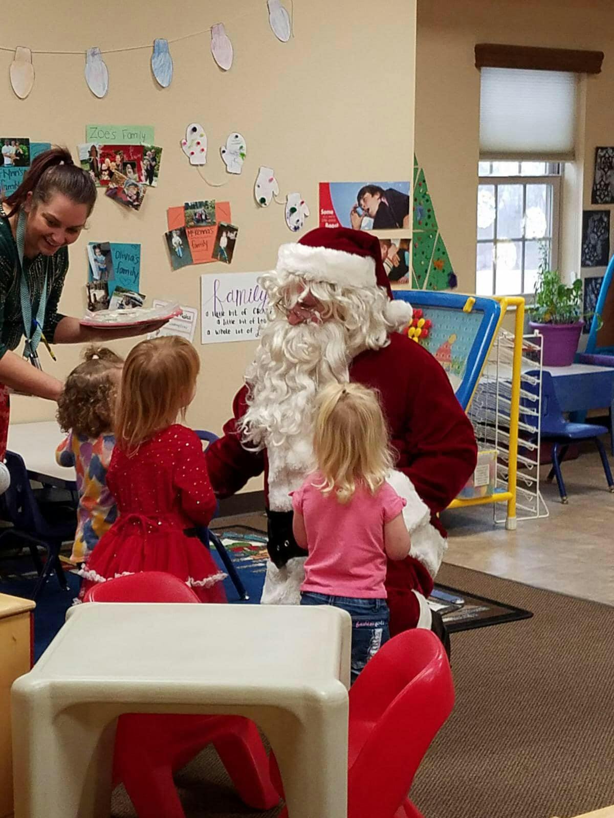 Person dressed as Santa Claus with children and an adult in a classroom