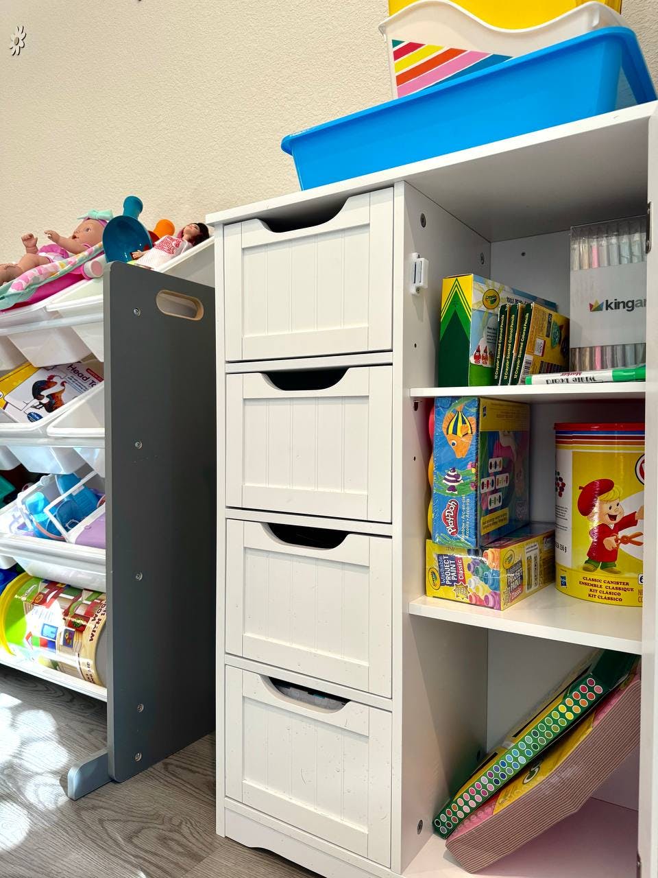 White storage unit with drawers and shelves filled with toys and art supplies
