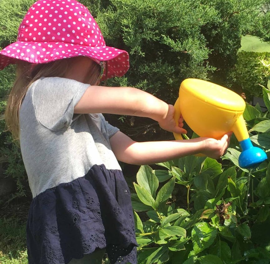 Child in a polka dot hat watering plants with a yellow watering can