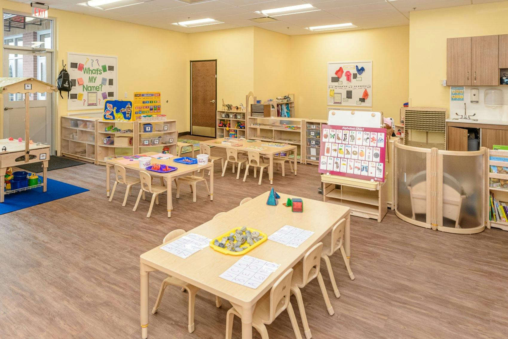 An empty classroom with multiple small tables, chairs, and learning materials