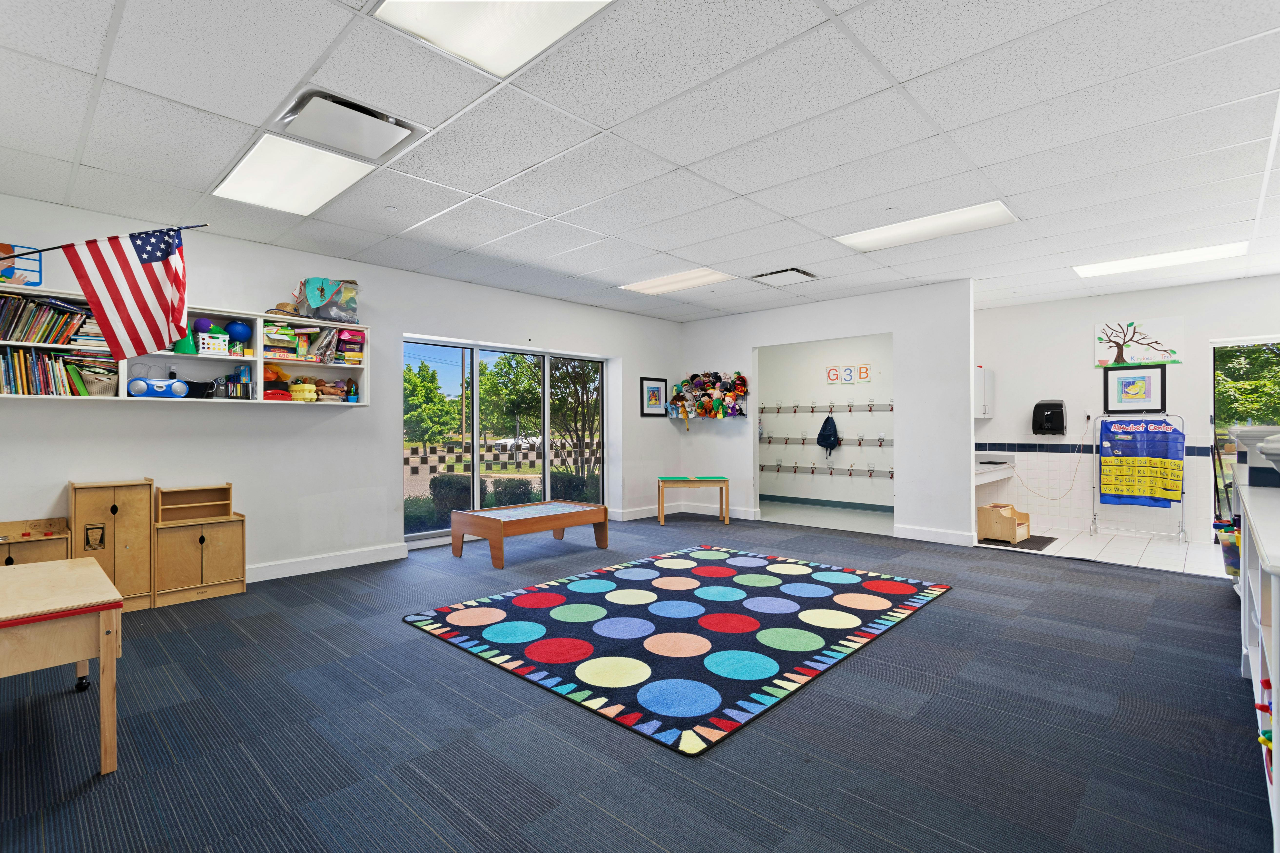 Classroom with colorful rug, low wooden furniture, bookshelves, and a window