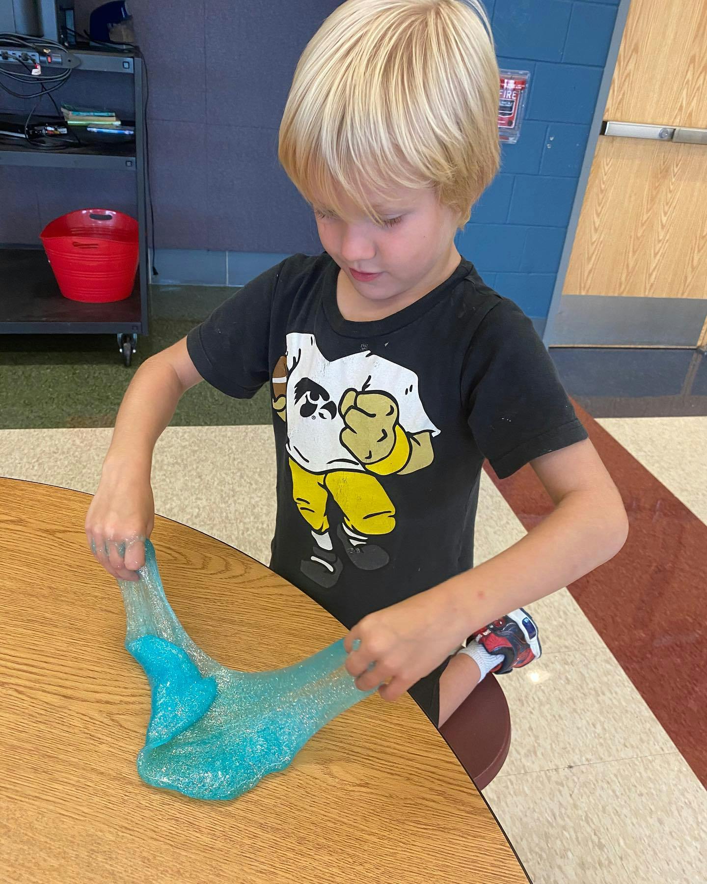 Child stretching blue glitter slime on a wooden table