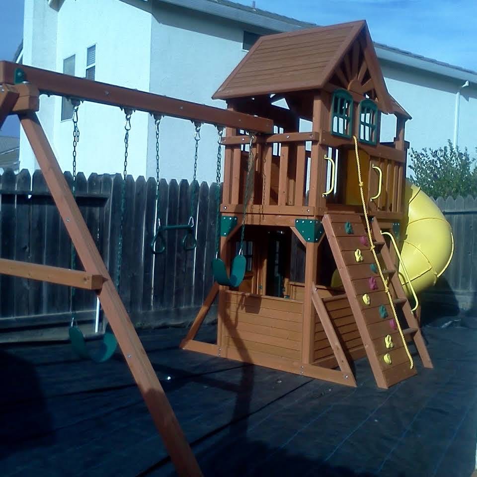 Wooden playground set with swings, slide, and climbing wall