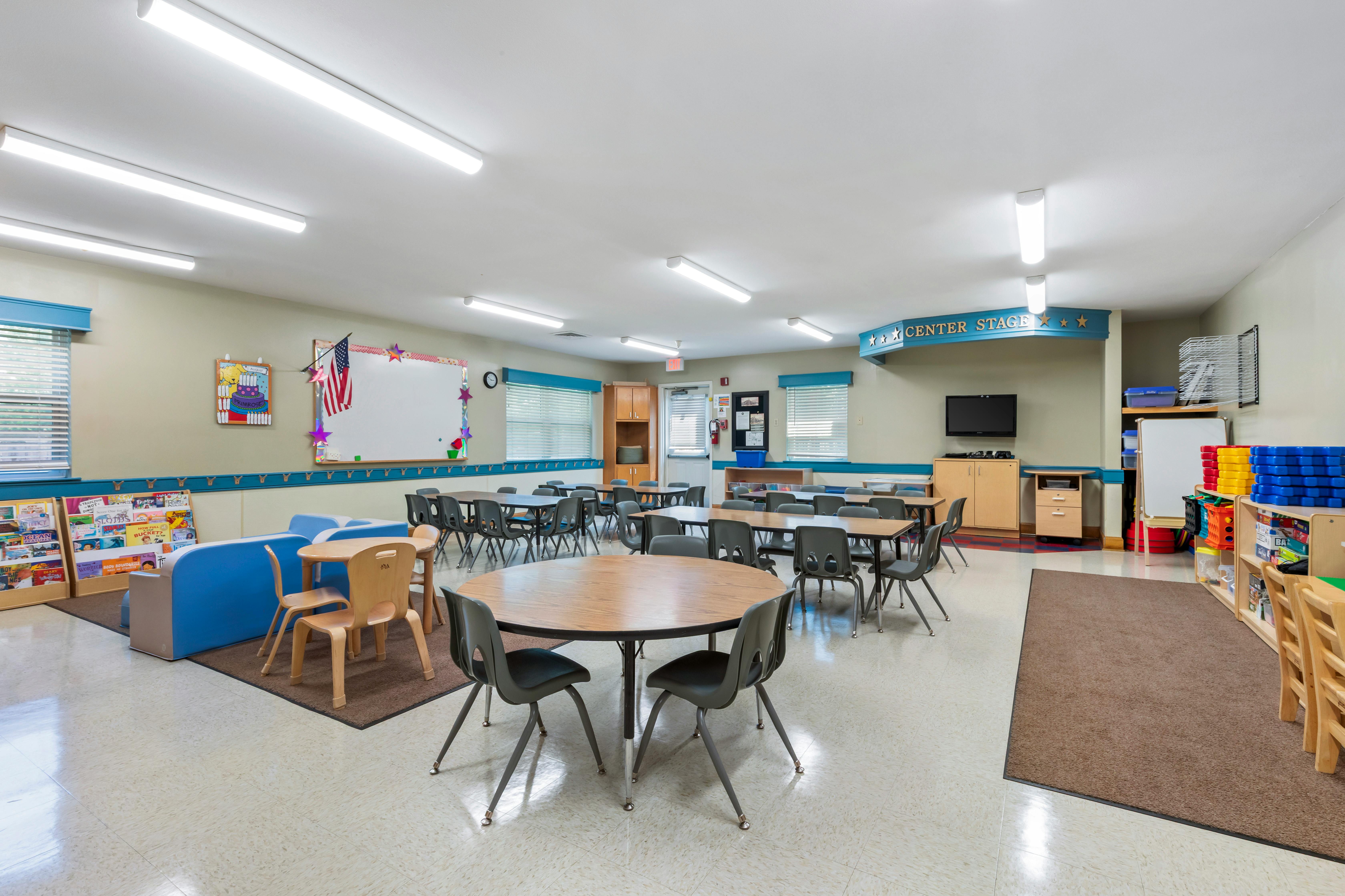 Classroom with children's tables and chairs, play area with books and blue seating