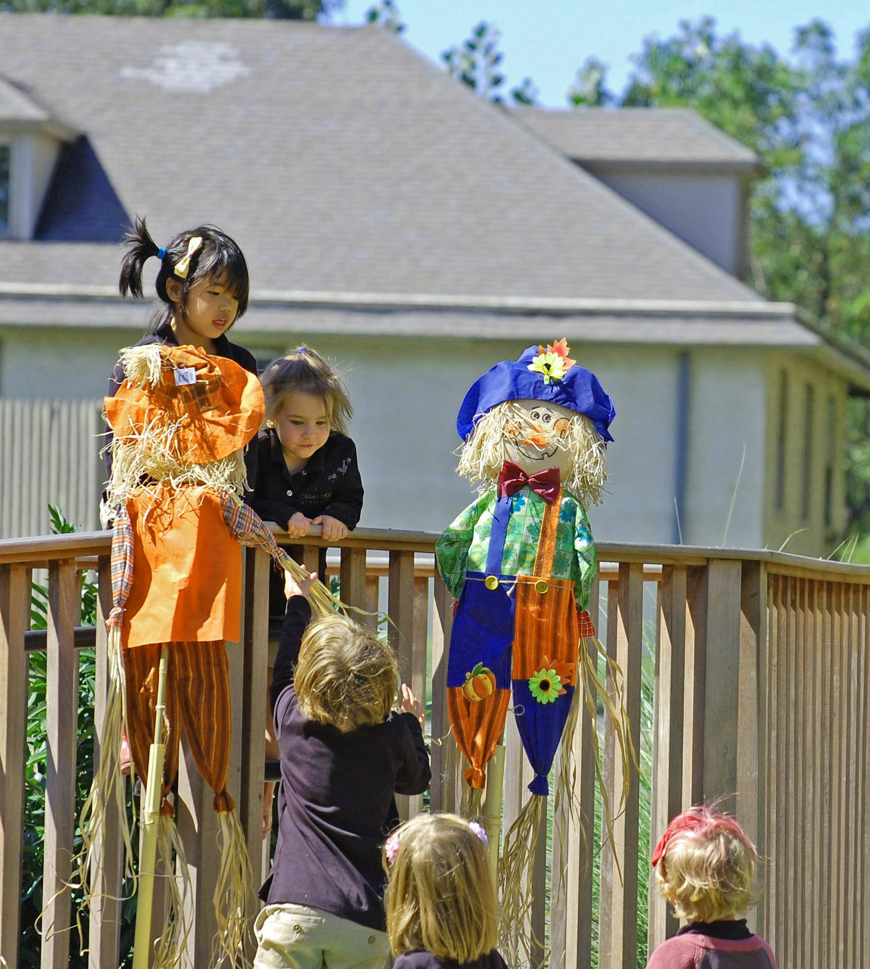 Children interacting with scarecrows on a wooden fence