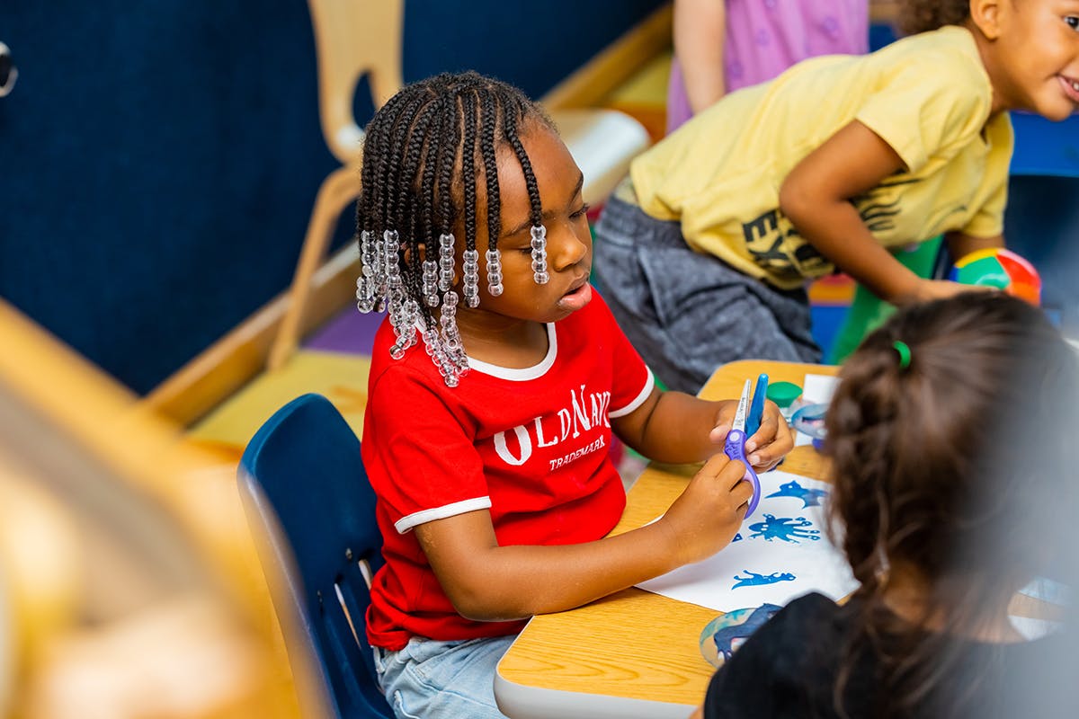 Child in red shirt cutting paper with scissors at a table
