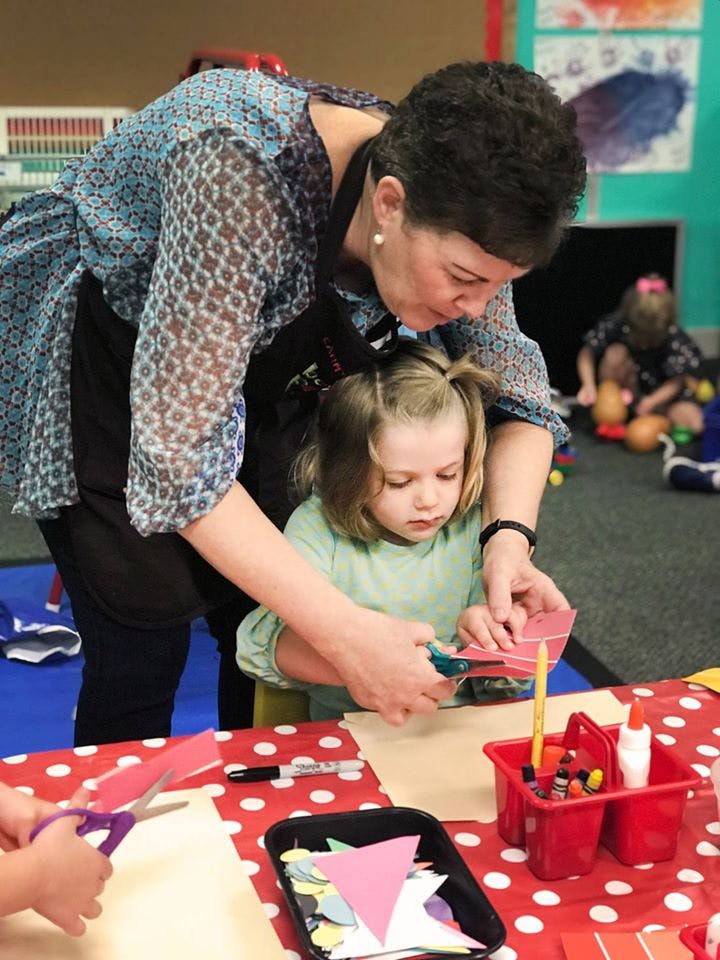 Adult helping a child cut paper with scissors