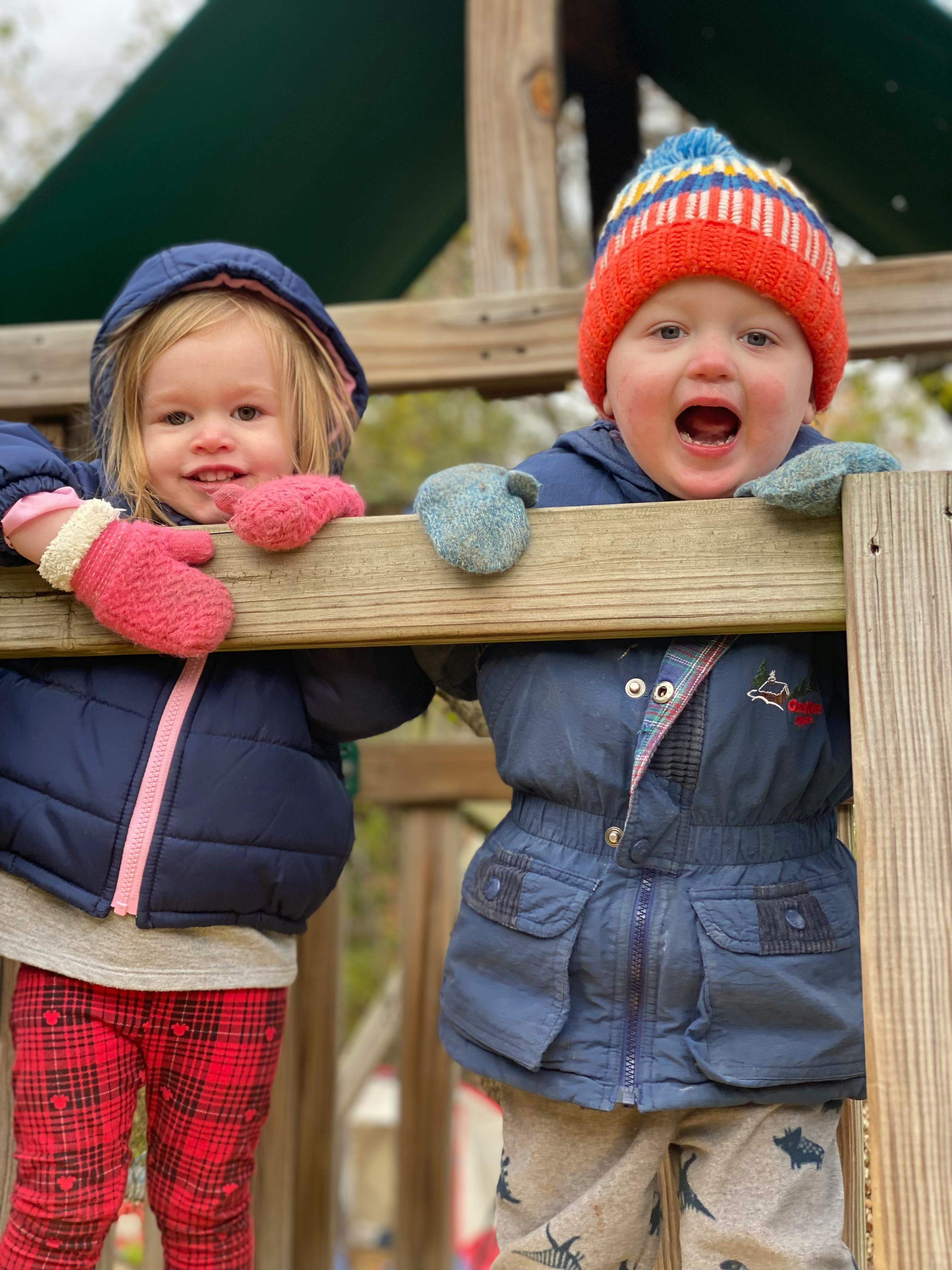 Two children in winter clothes on a wooden play structure