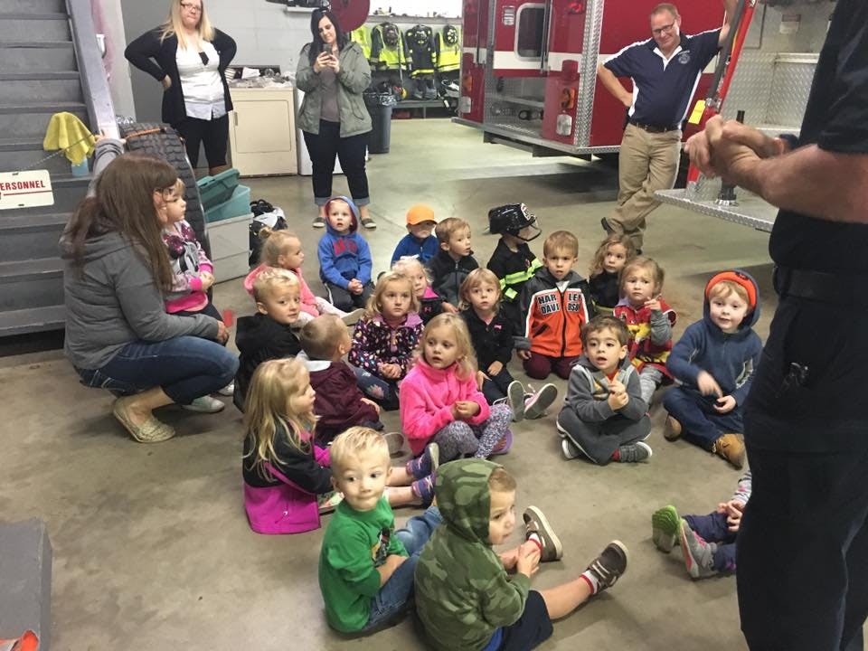 Adults and children sitting on the floor in a room with a fire truck
