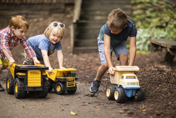Three children playing with toy dump trucks outdoors