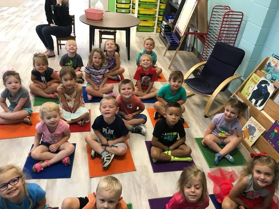 Many children sitting on colorful mats in a classroom
