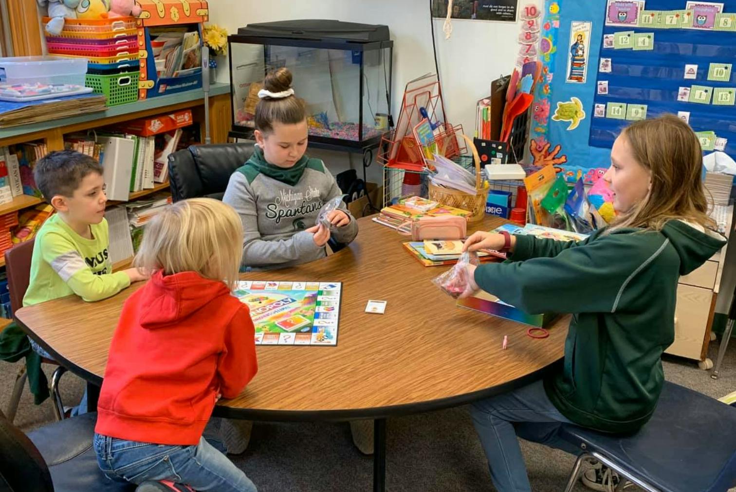 Four children sitting around a table playing a board game in a classroom