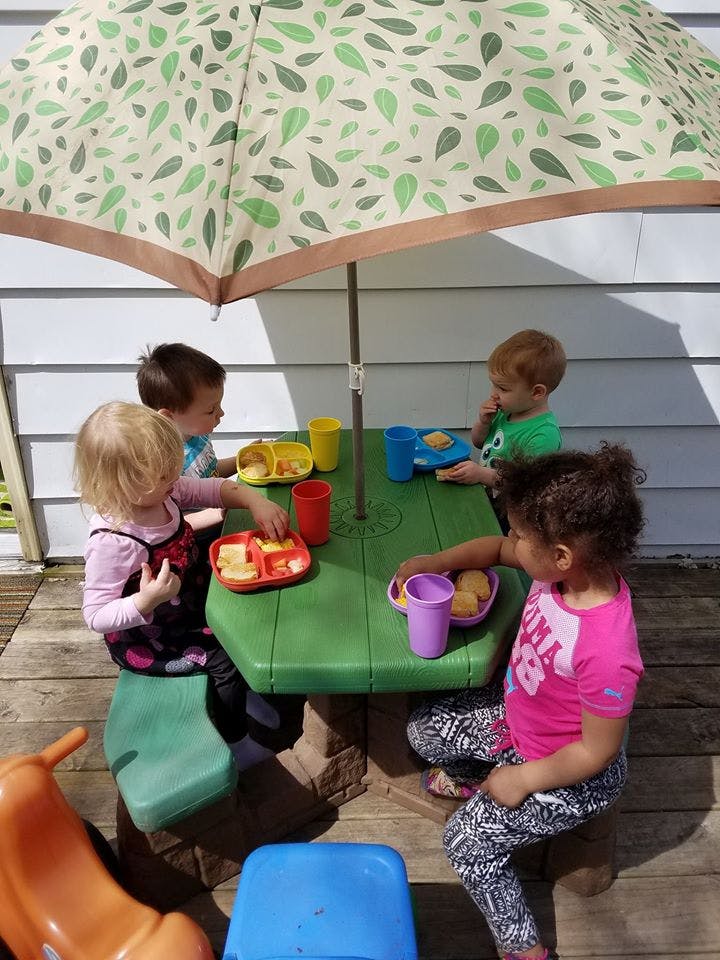 Children eating snacks at a small picnic table under an umbrella