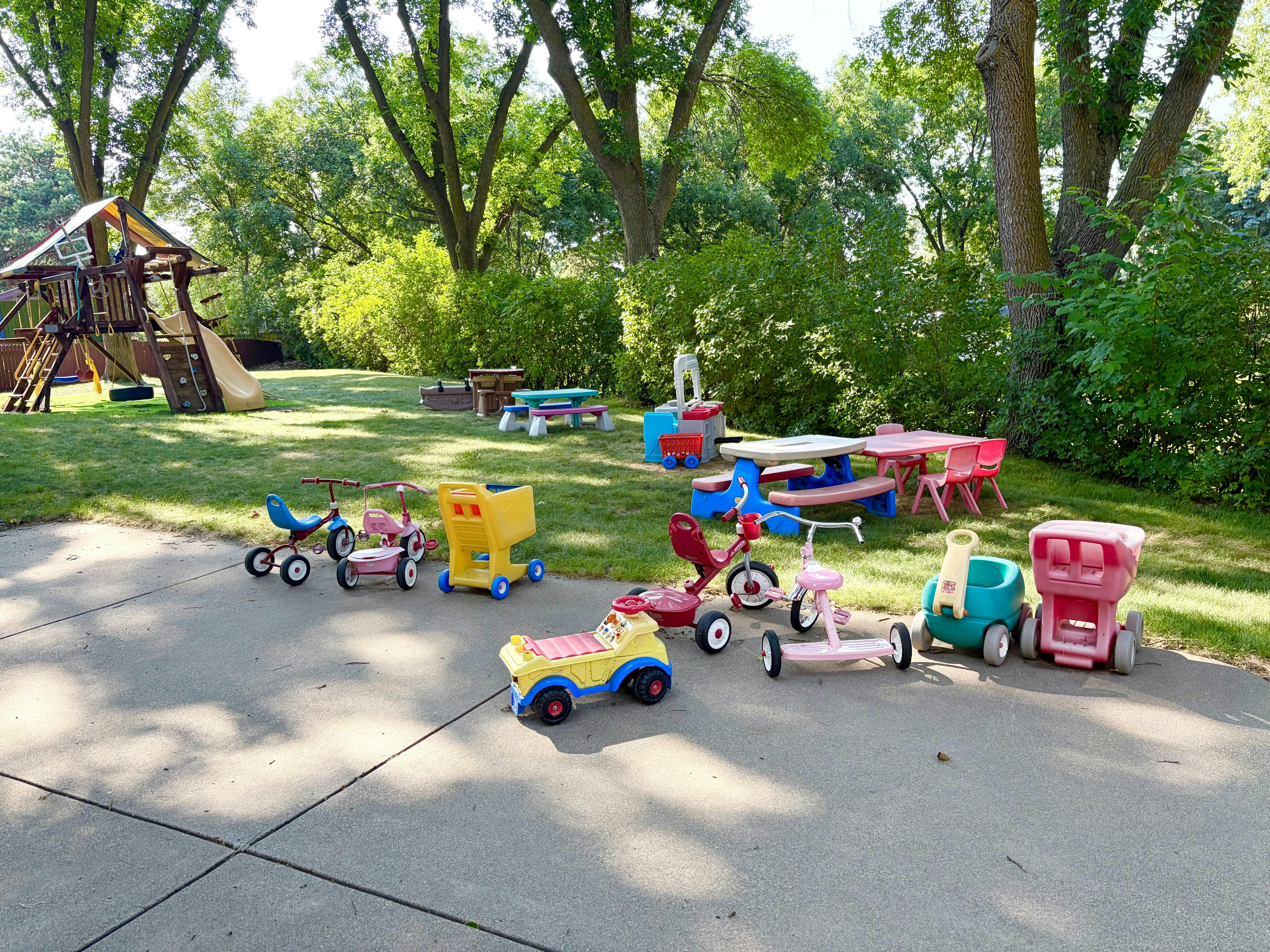 Plastic ride-on toys parked on a concrete patio next to a grassy playground