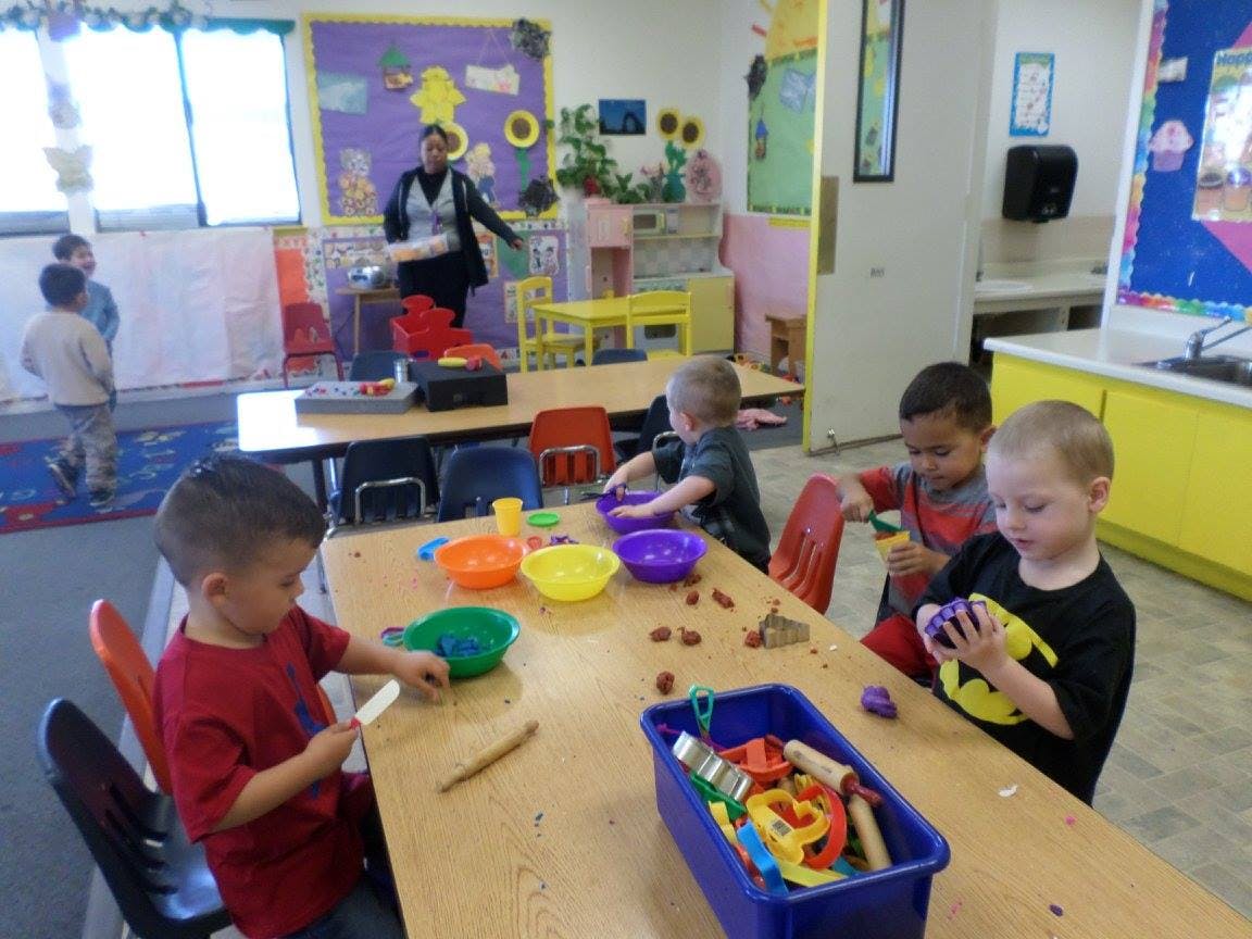 Children playing with bowls and small objects at a table in a classroom