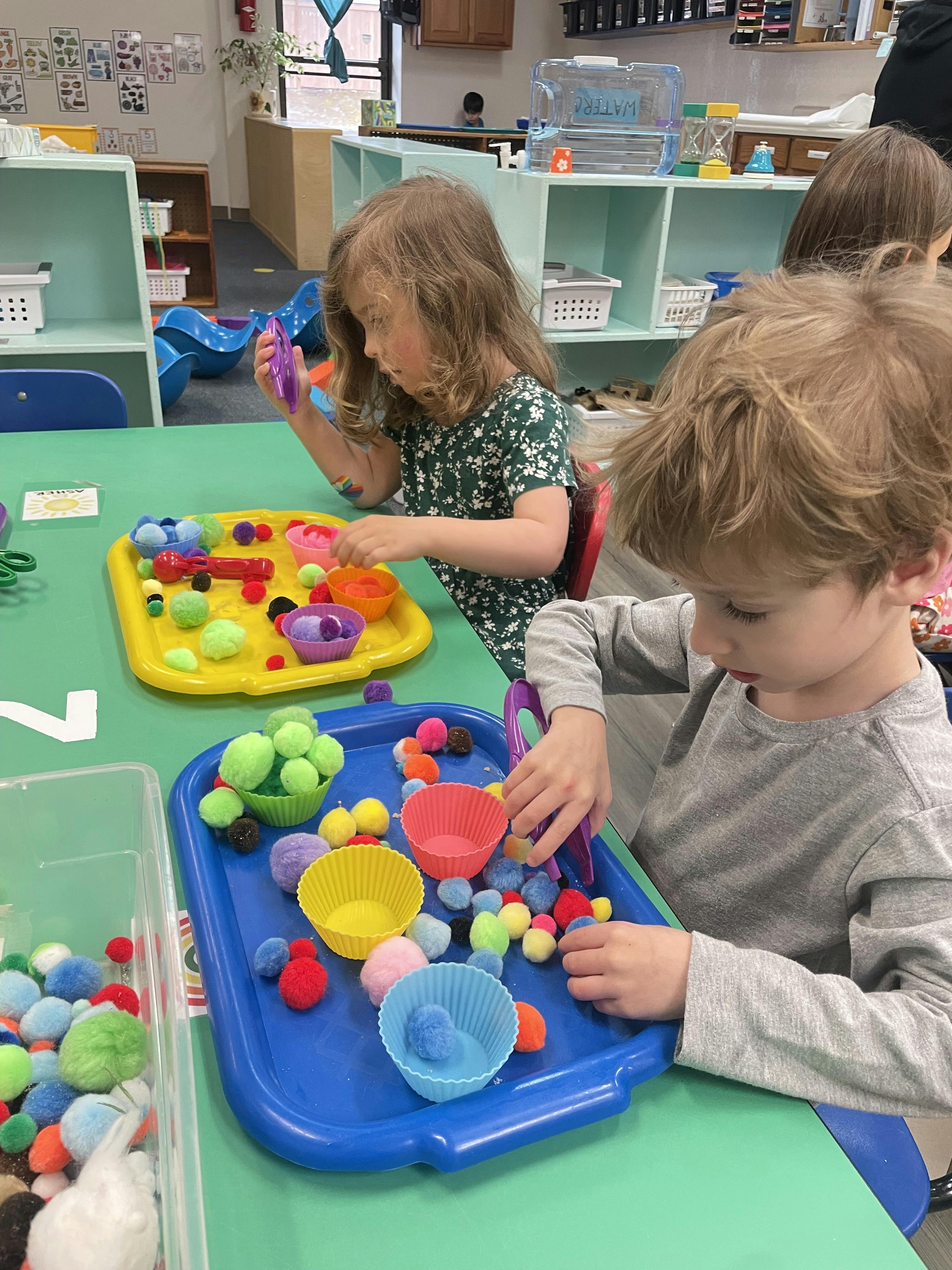 Two children playing with colorful pom-poms and small cups at a table