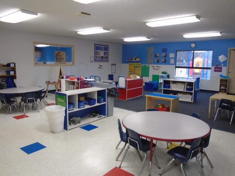 A classroom with small tables, chairs, and play areas