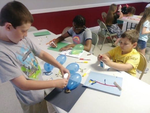 Children doing crafts with balloons and paper at a table