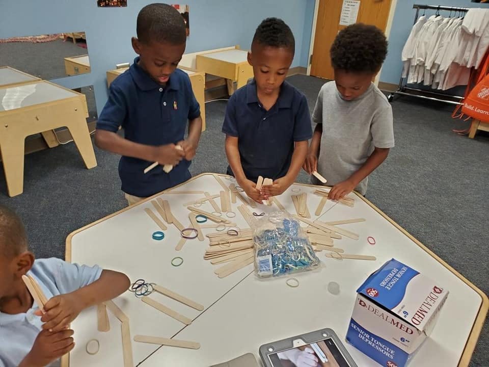 Four children working with craft sticks and rubber bands at a table