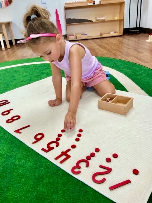Child placing counters next to wooden numbers on a rug
