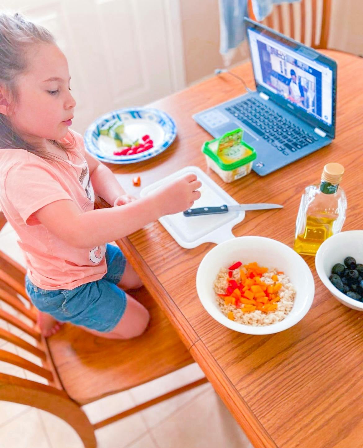 Child cutting food on a cutting board at a table with a laptop