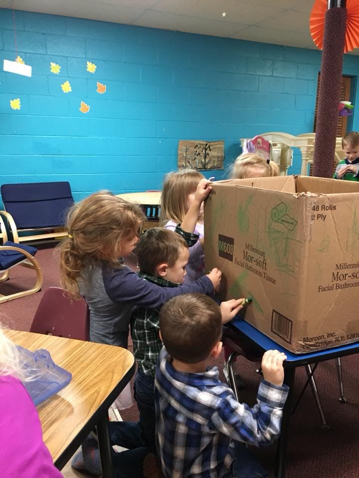 Children drawing on a large cardboard box in a classroom
