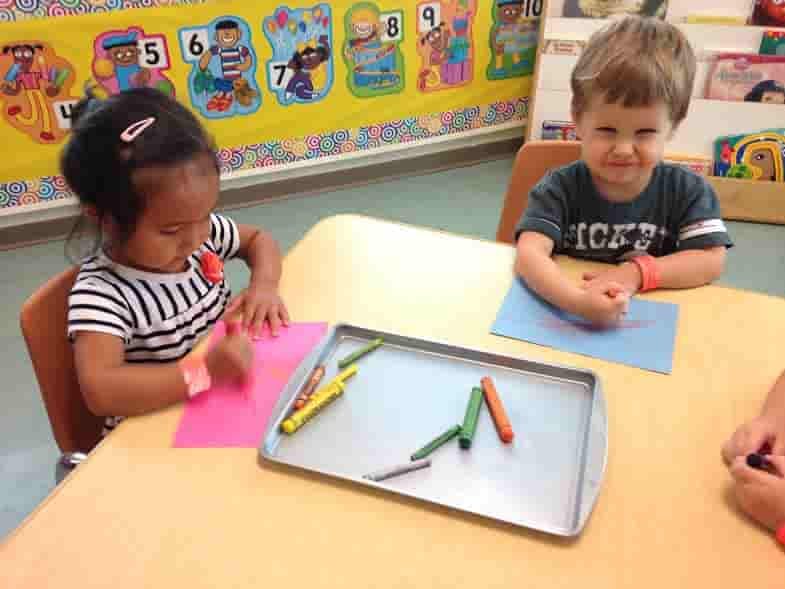 Two children at a table with crayons and paper in a classroom