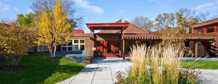 Building exterior with red doors and a walkway, surrounded by trees and grass
