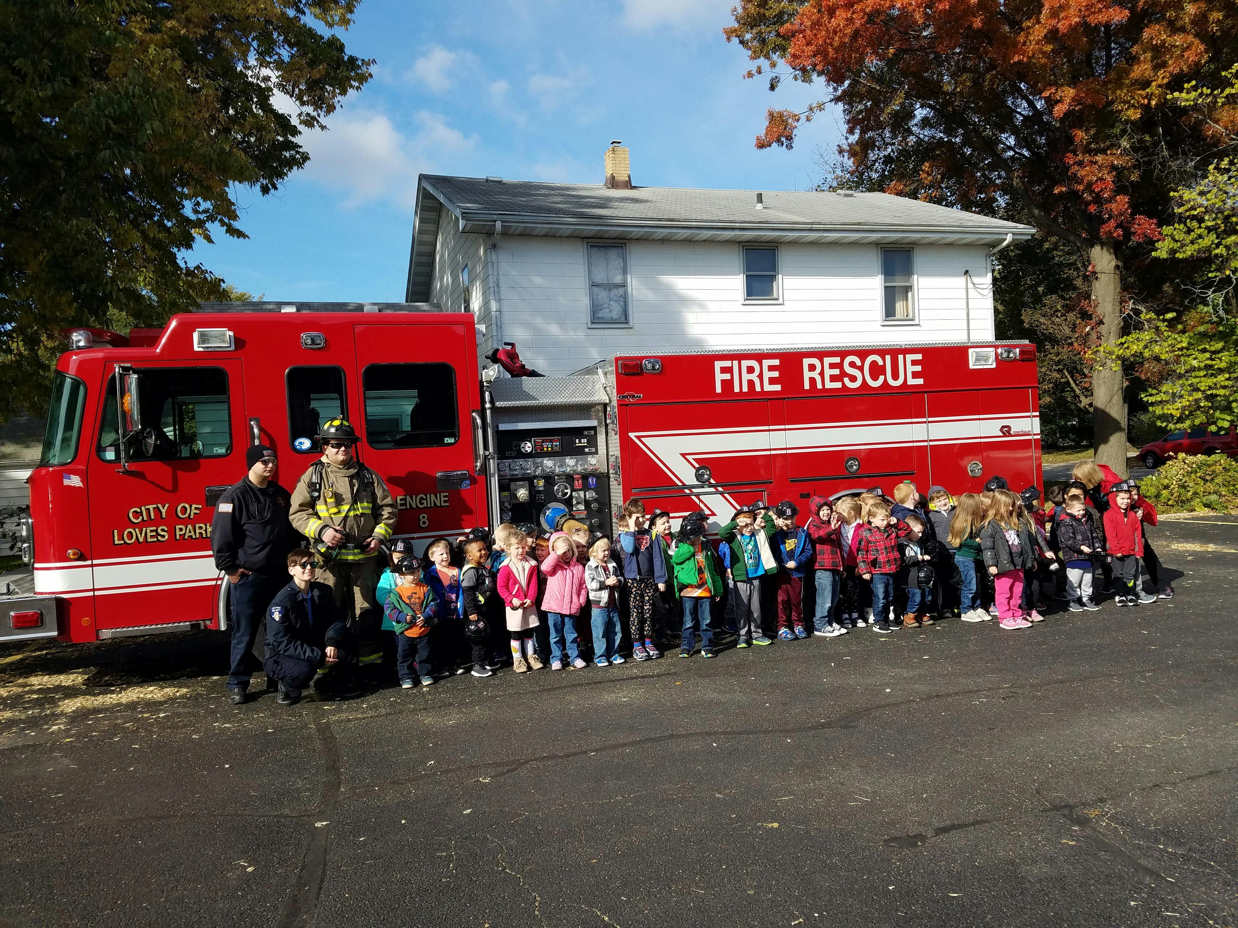 Firefighters and children standing in front of a fire truck and ambulance