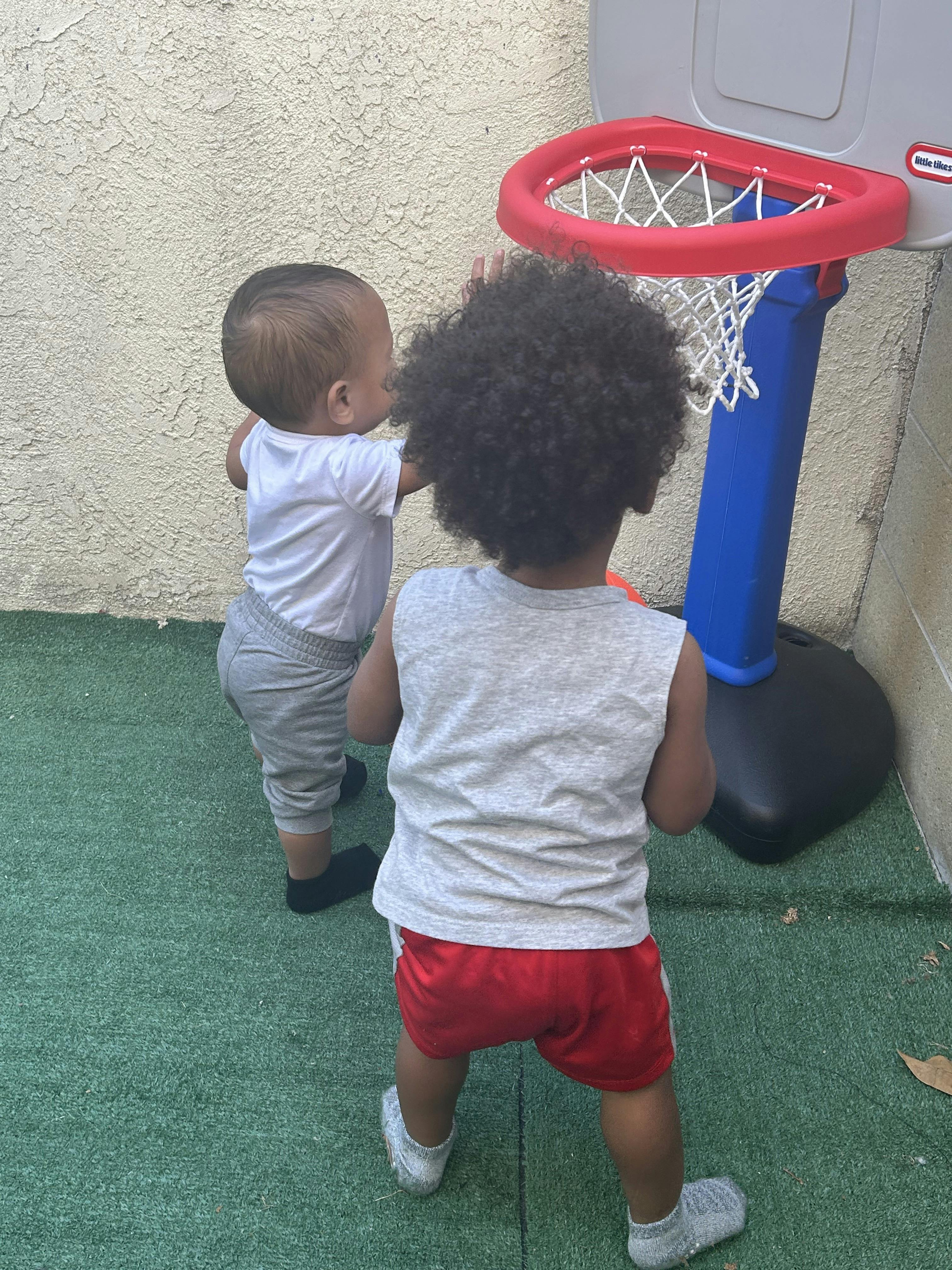 Two children standing in front of a toy basketball hoop