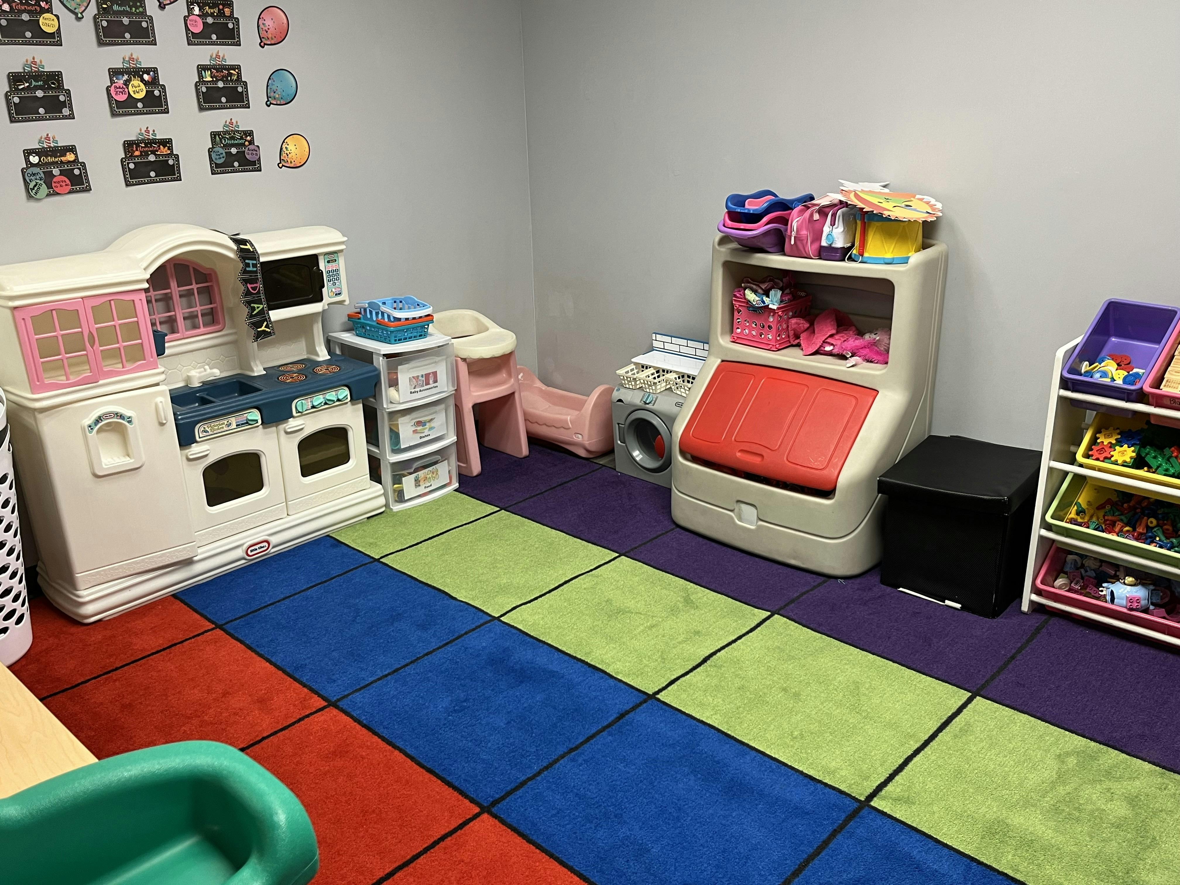 Child's playroom with toy kitchen, storage units, and colorful block rug