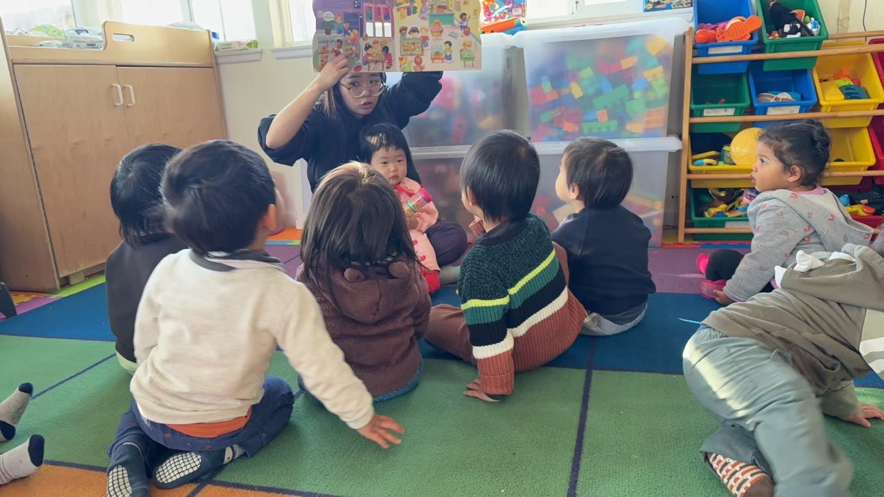 Person reading a book to a group of children in a classroom