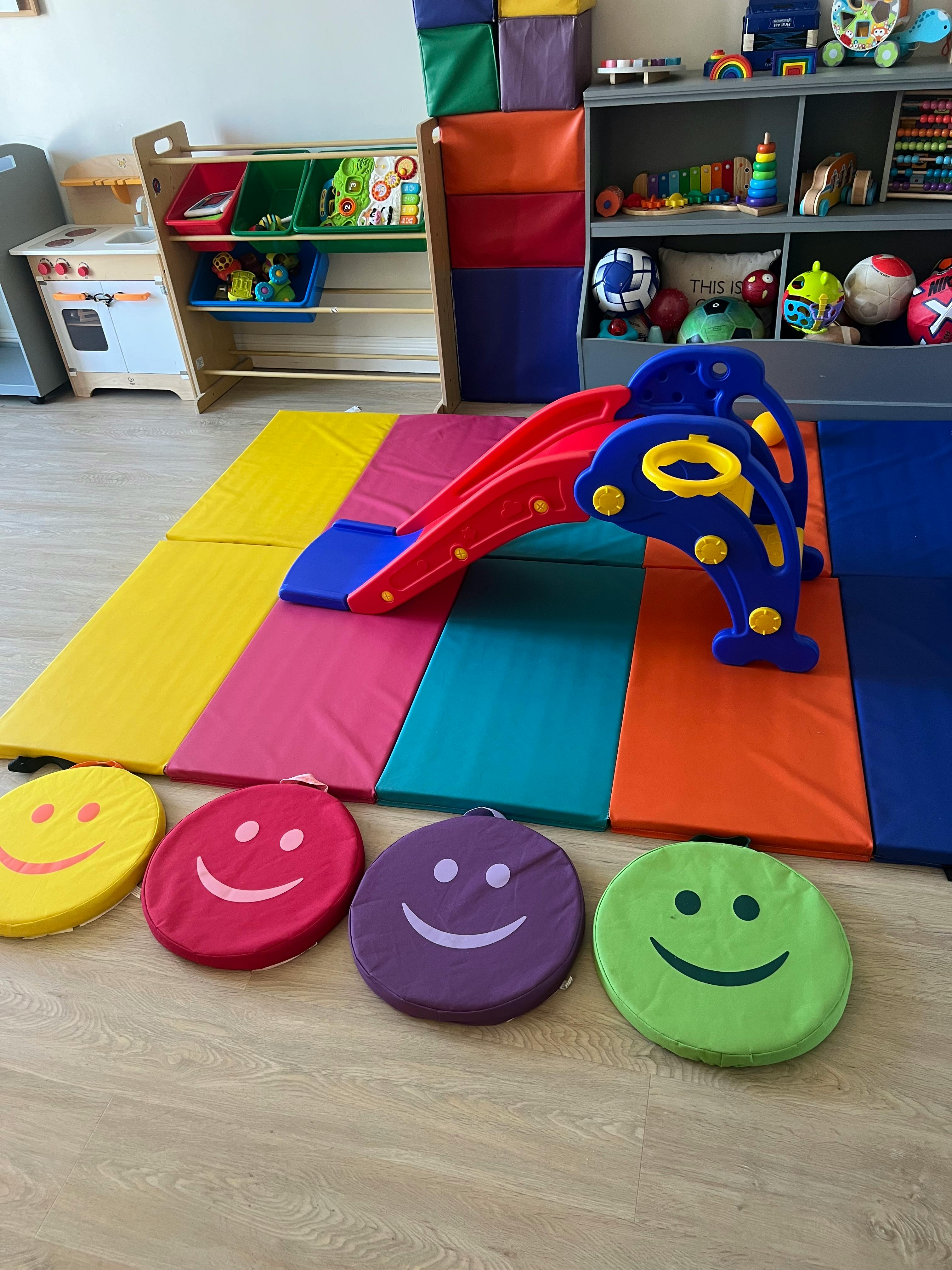 Indoor play area with a small slide, colorful mats, and smiley face cushions