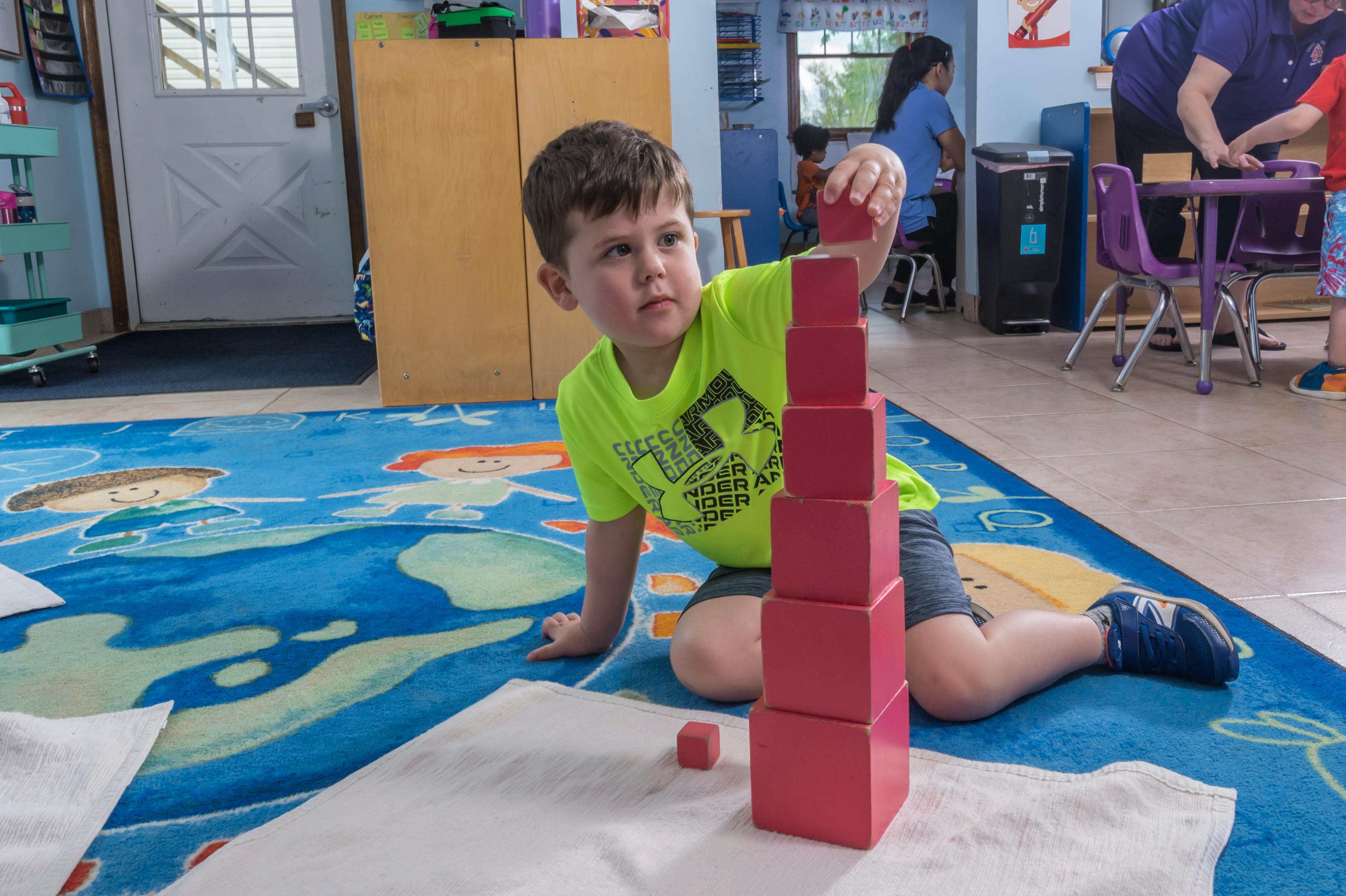 Child building a tower with red blocks in a classroom