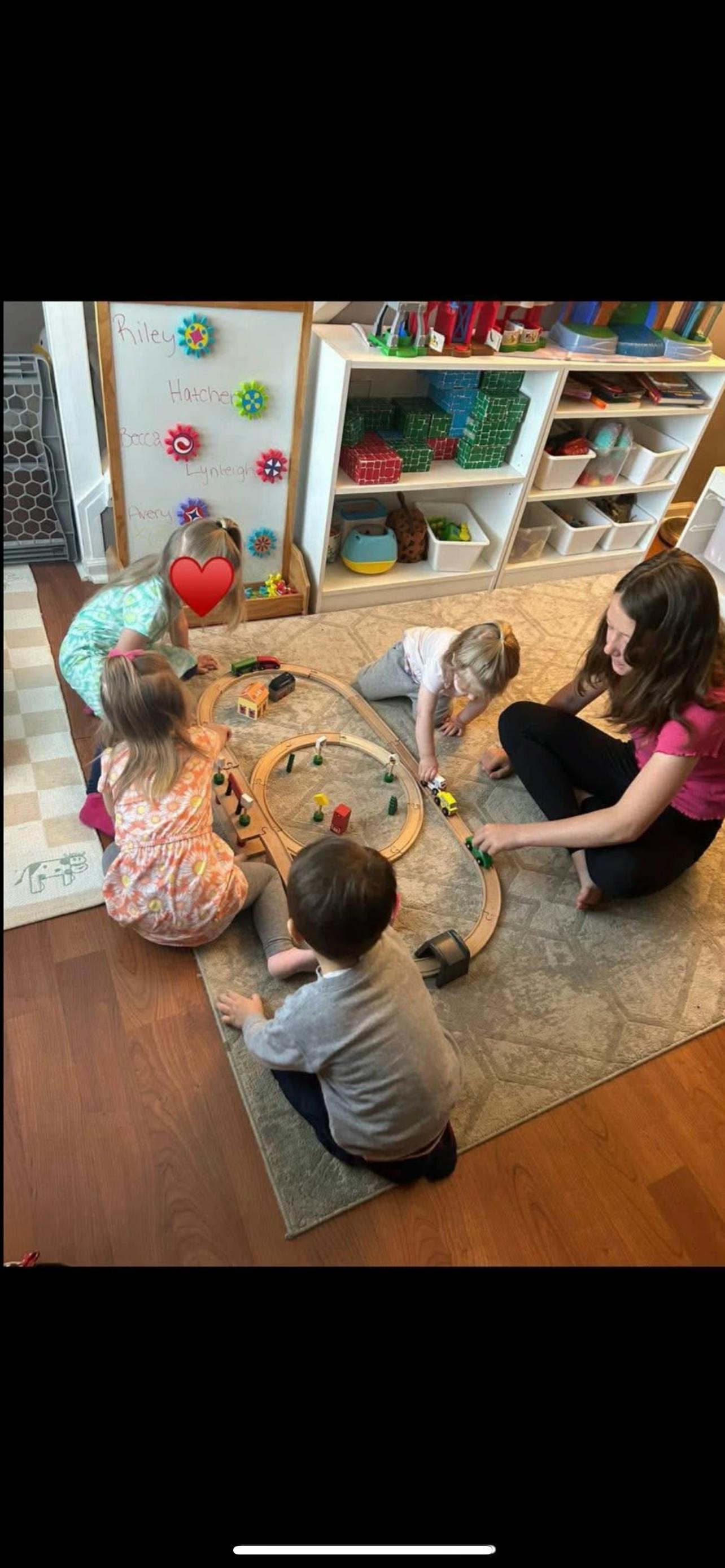 Adult and children playing with a wooden train set on a rug