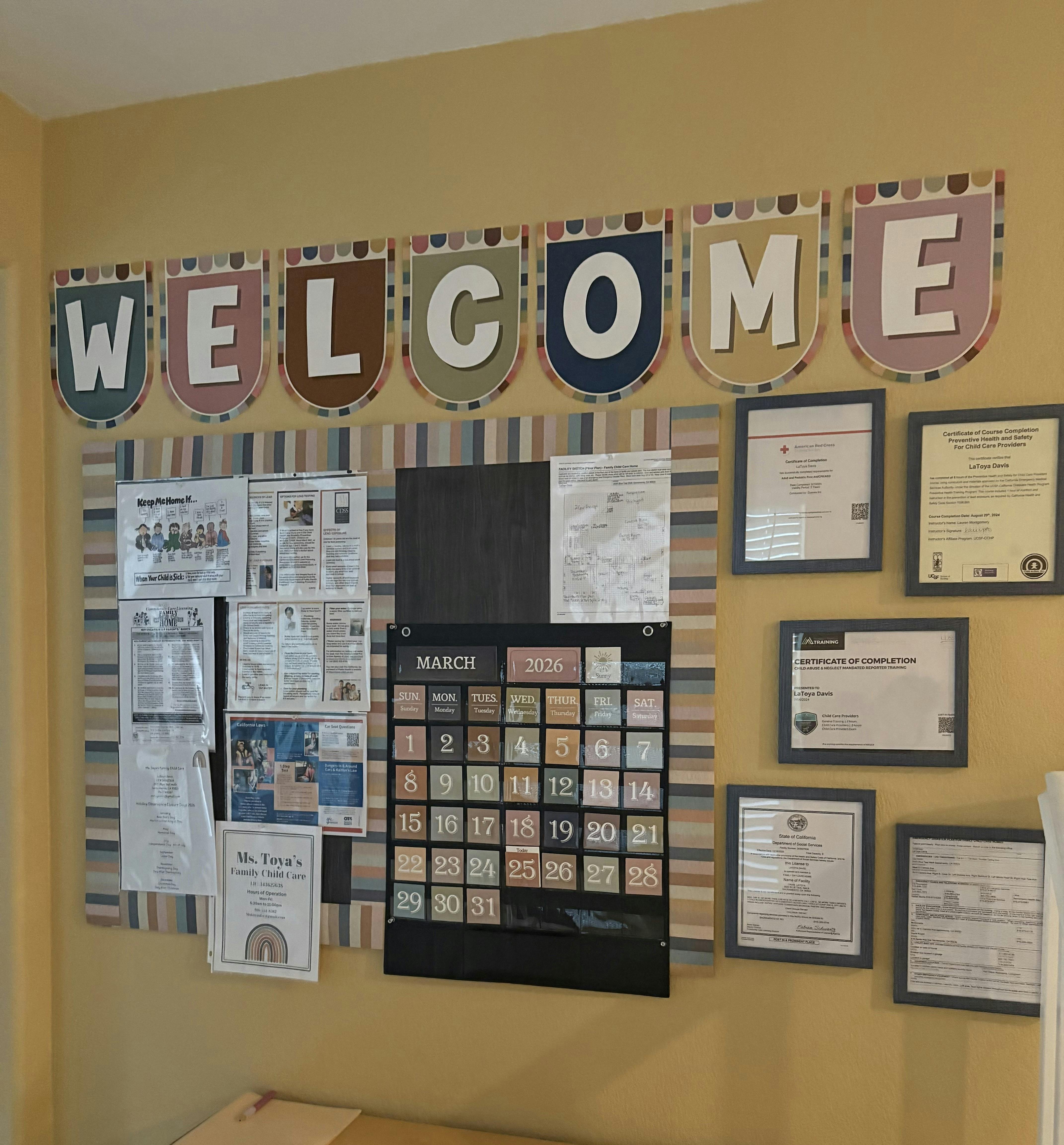 A wall display with a "WELCOME" banner, a bulletin board, a March 2026 calendar, and framed certificates