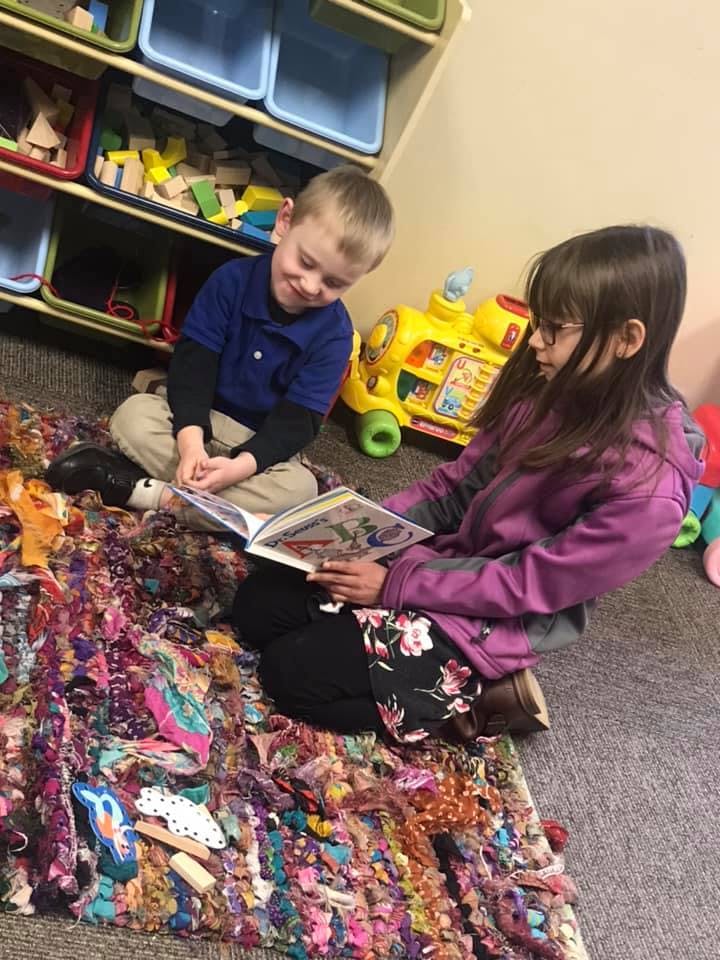 Two children sitting on a rug, one reading a book