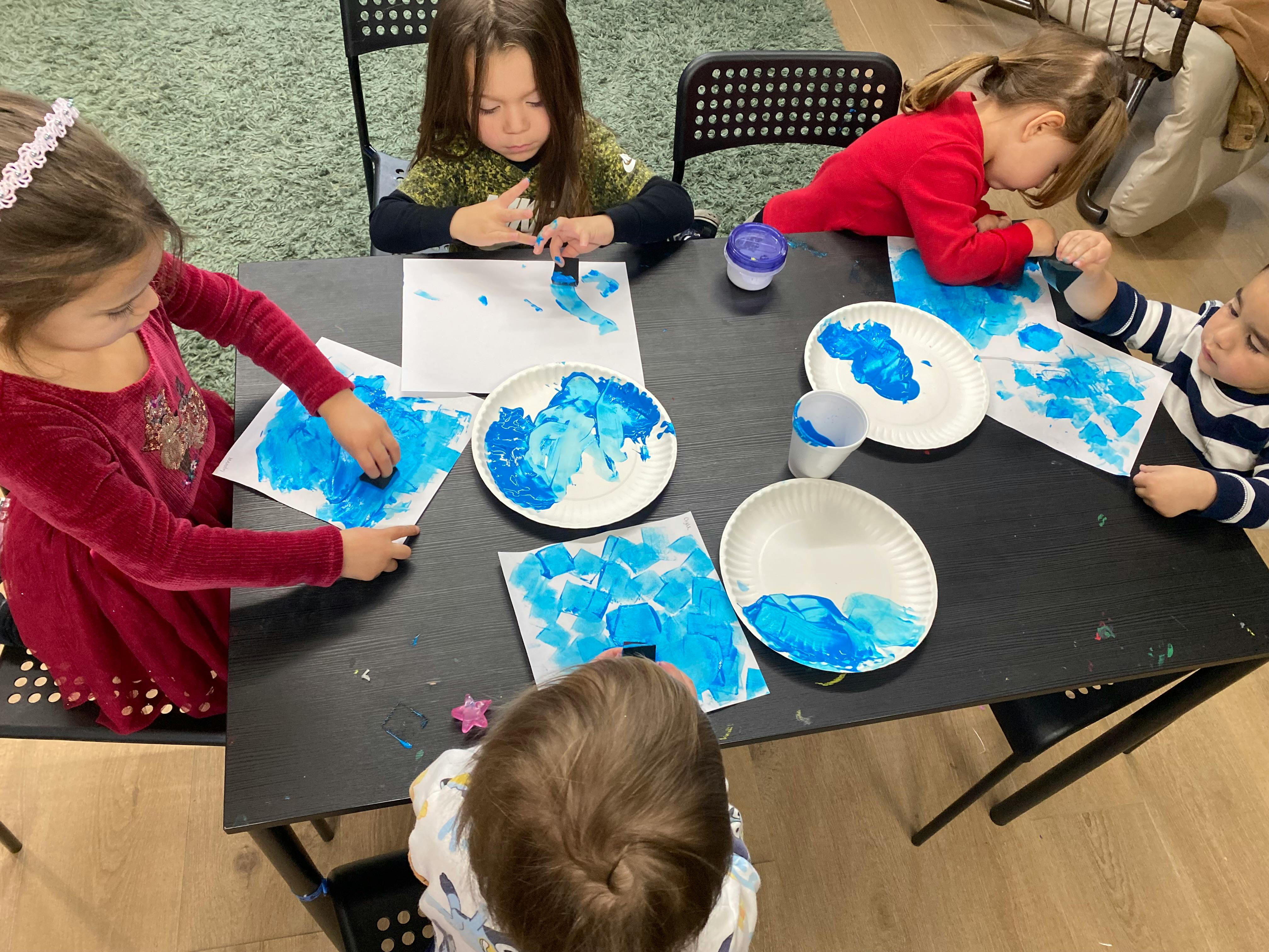 Children painting with blue paint at a table