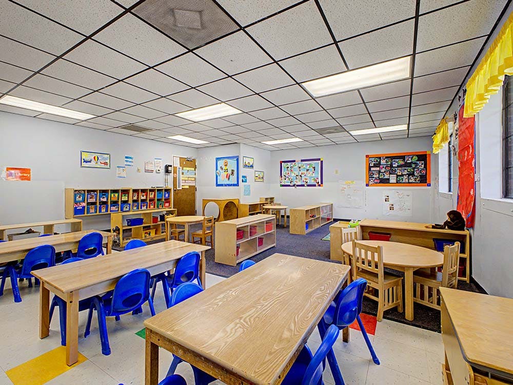 Classroom with wooden tables, blue chairs, and children's artwork on the walls
