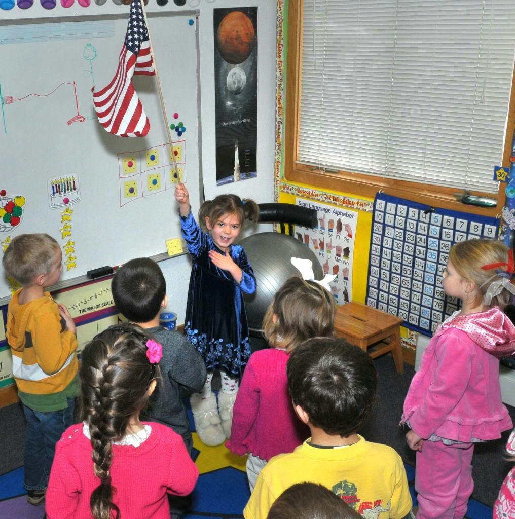 Child holding an American flag in front of other children in a classroom