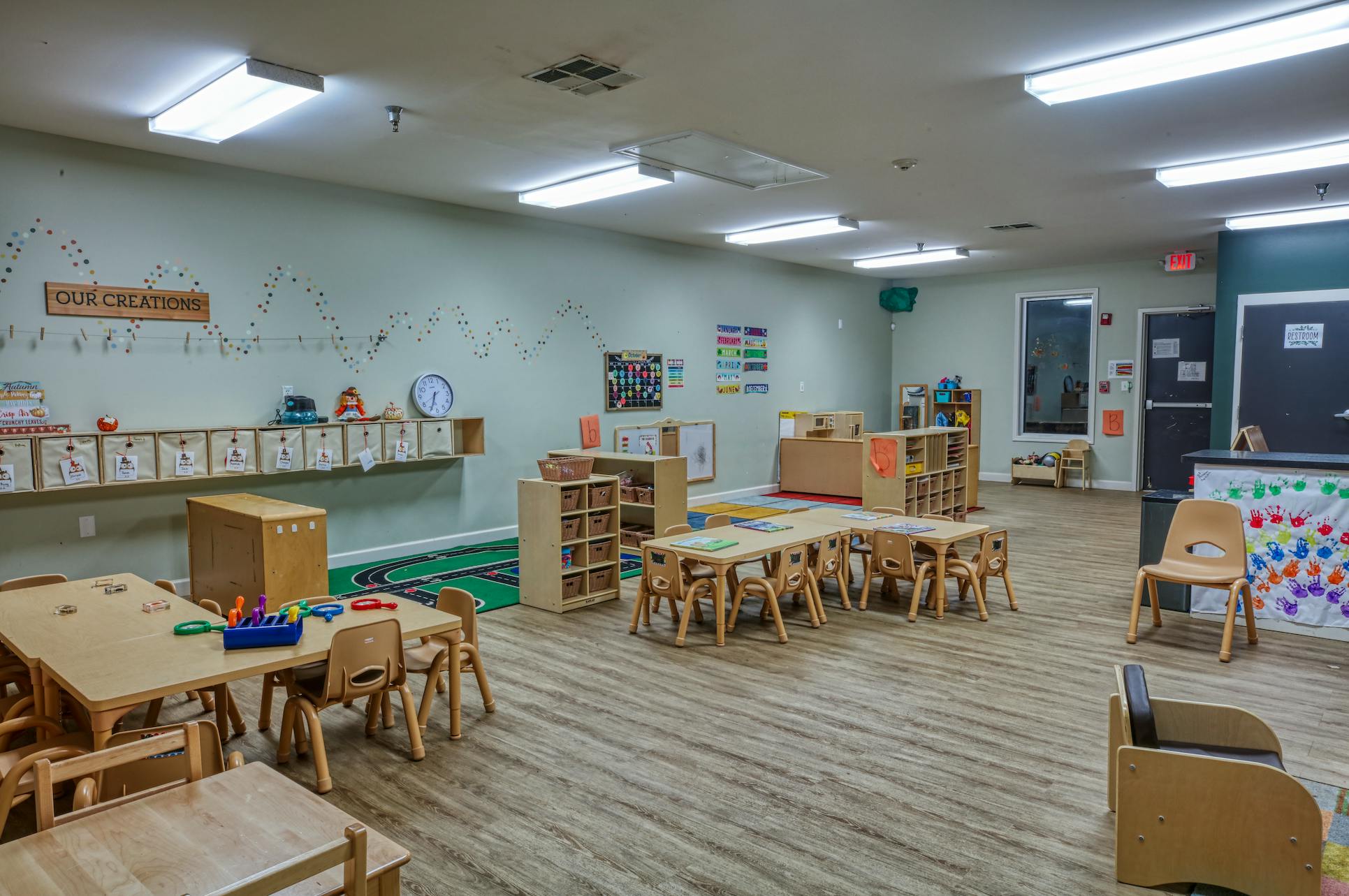 Classroom with small tables and chairs, cubbies, and decorations on the wall "OUR CREATIONS"