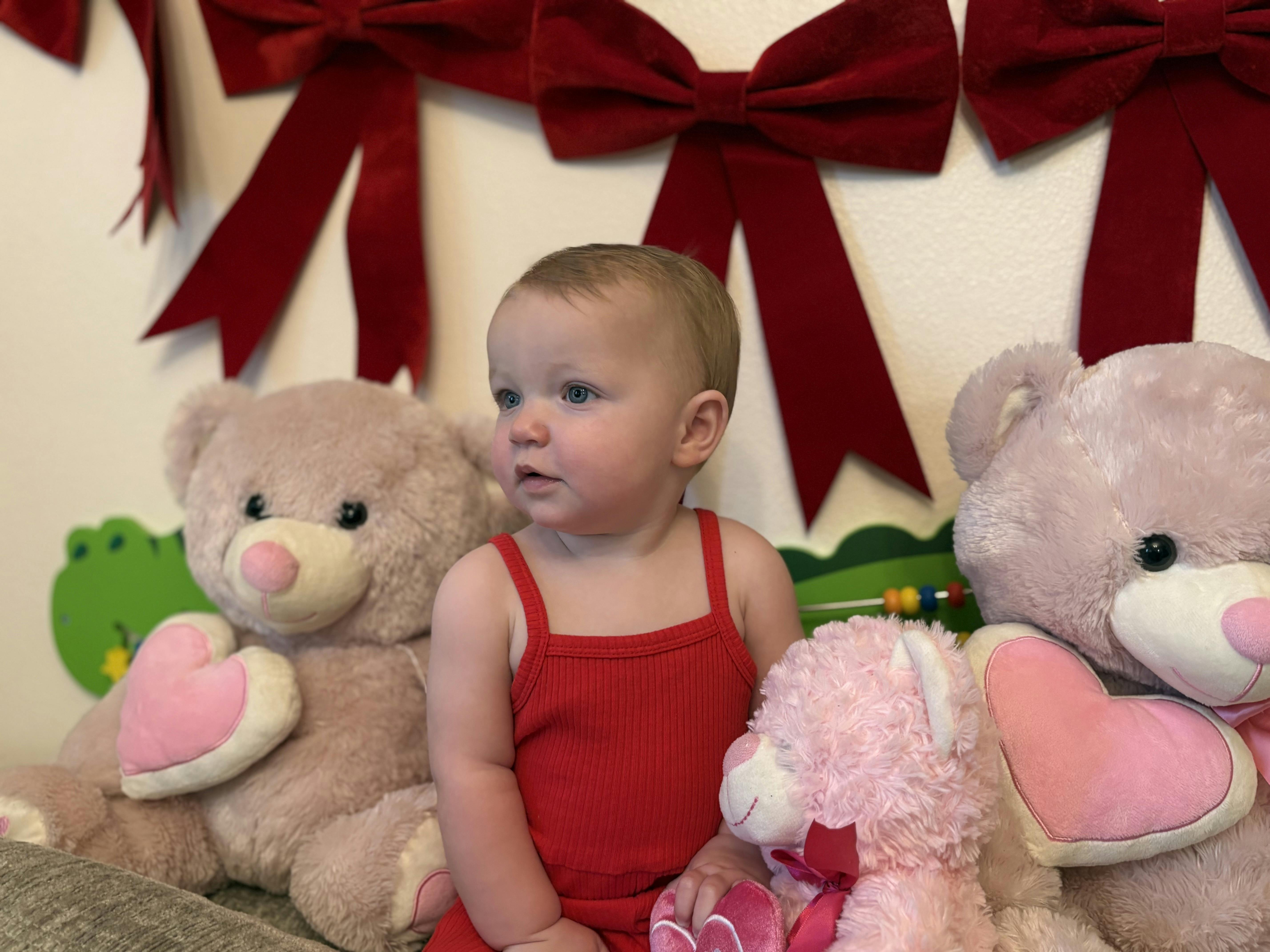 Child sitting between two teddy bears, wearing red